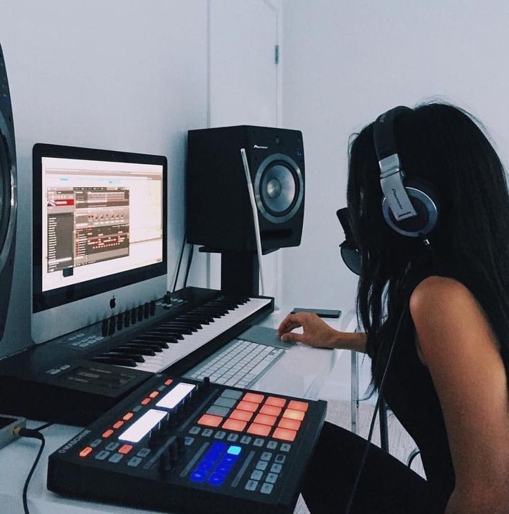 a woman sitting in front of a computer with headphones on and music equipment around her