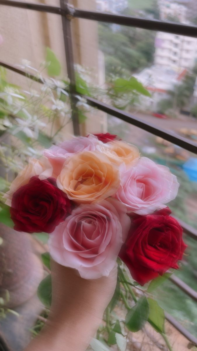 a person holding a bouquet of flowers in their hand near a window with the city outside