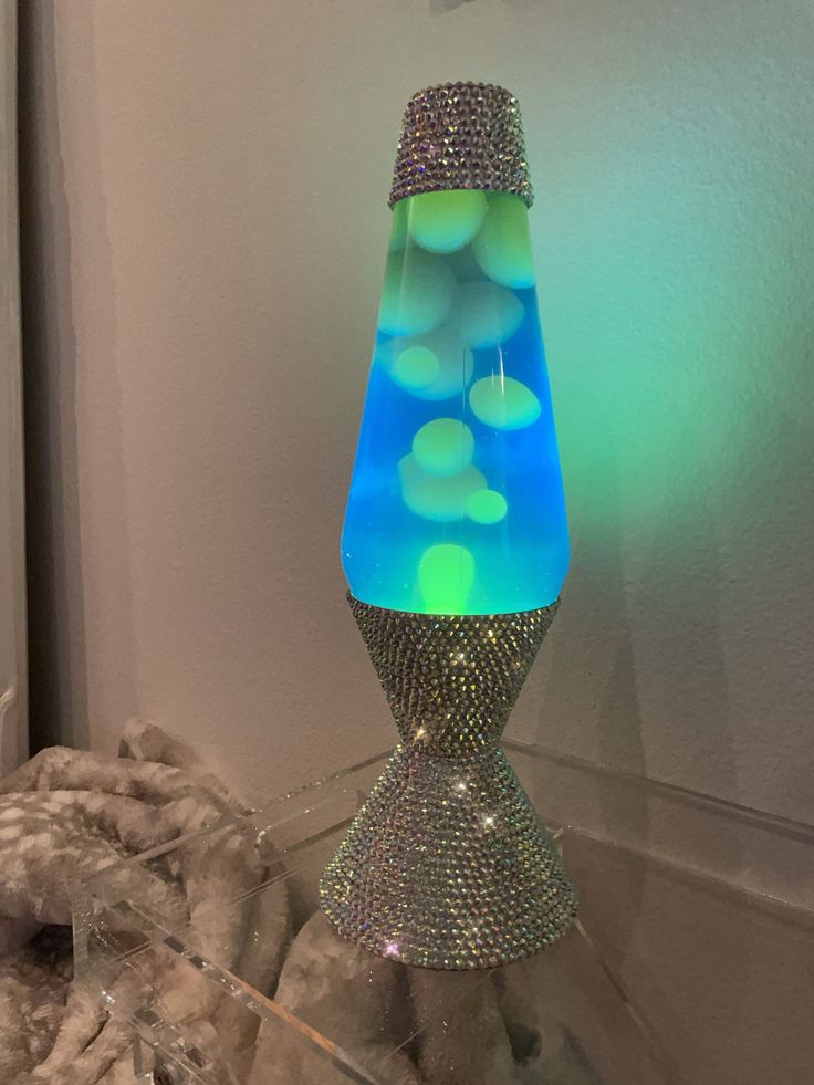 a blue and green vase sitting on top of a glass table next to a white wall