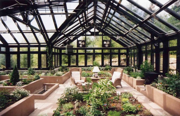 the inside of a glass house with lots of plants and flowers growing in it's center