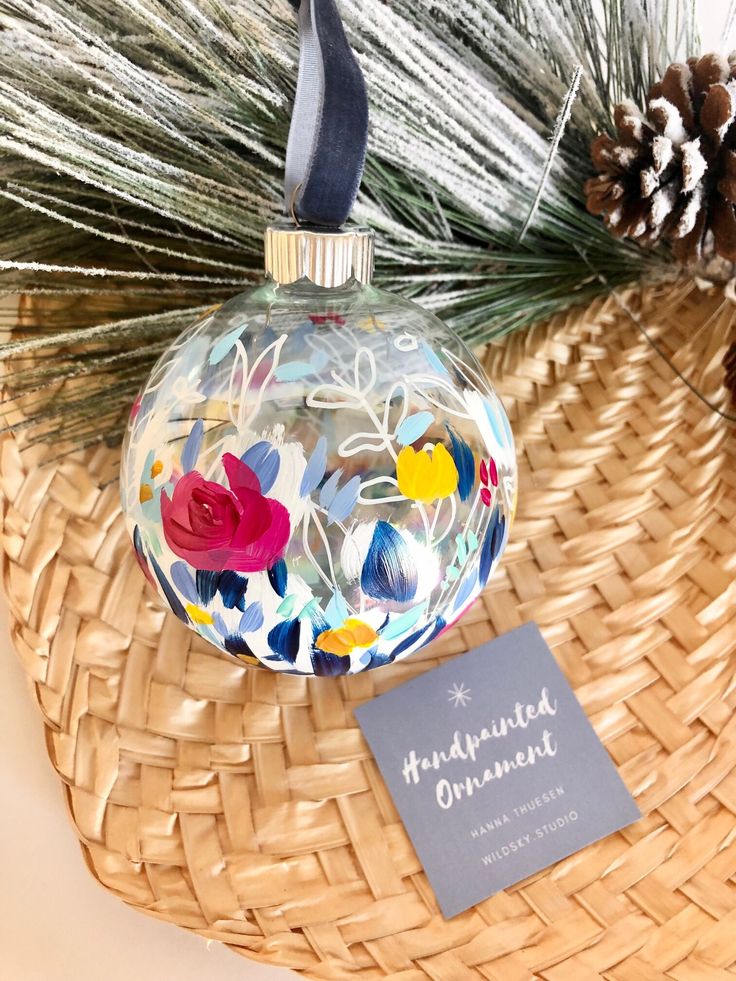 a glass ornament with flowers and pine cones in the background on a wicker basket