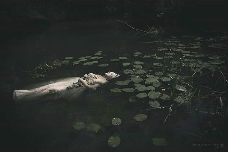 a woman is floating in the water with lily pads on her back and head down