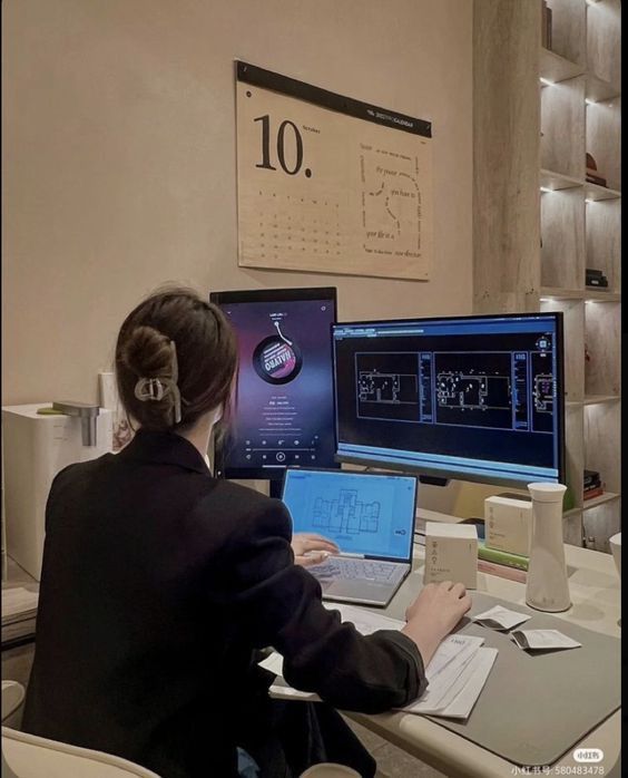 a woman sitting at a desk with two laptops and a desktop computer on it