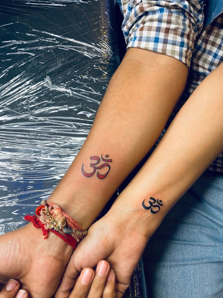 two people are holding hands with tattoos on their arms and the other one has an om symbol