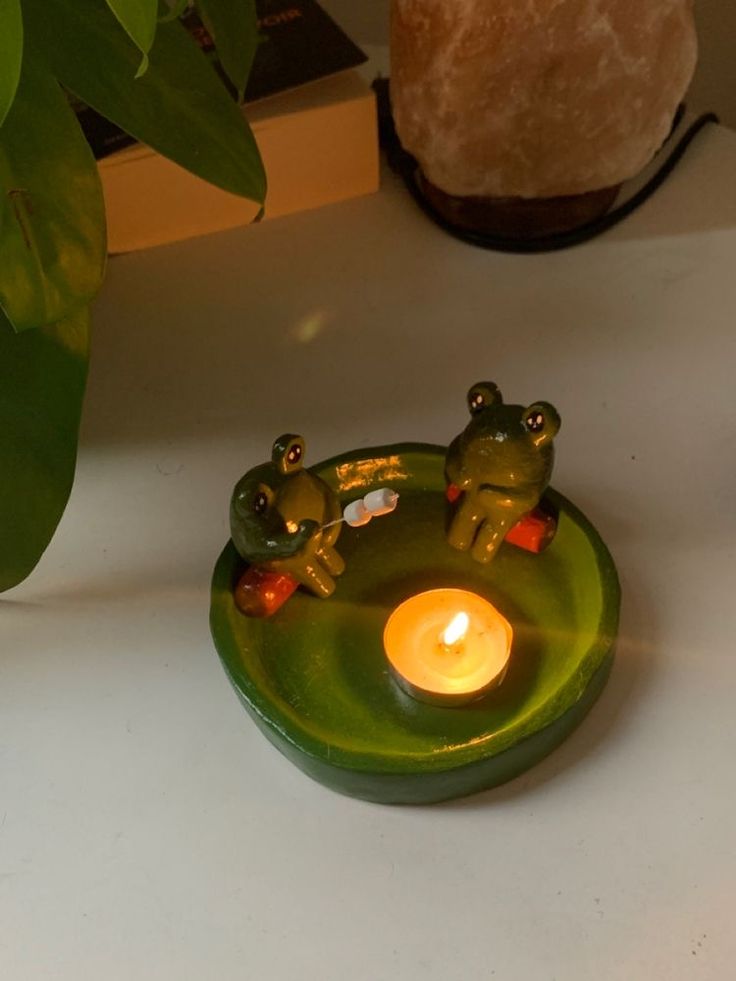 two frogs sitting on a green plate with a lit candle in the shape of a frog