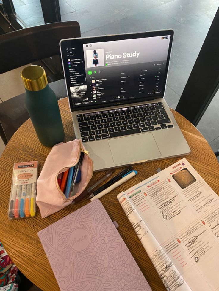 an open laptop computer sitting on top of a wooden table next to a notebook and pencils