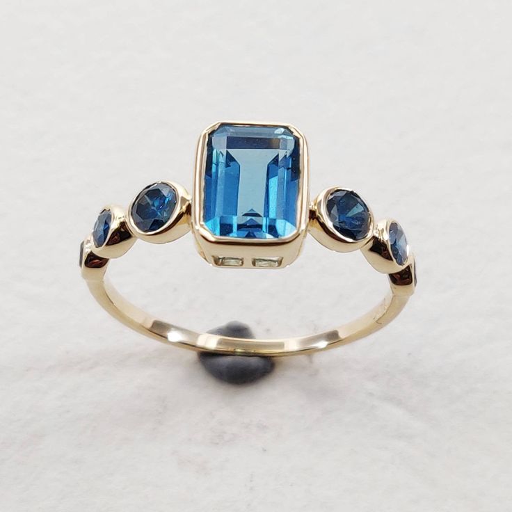 **KINDLY CHECK OUT THE VIDEO OF THE ITEM FOR A CLEARER VIEW**Details of the ring Gemstone: Center Gem: London blue topaz Side Gem: Blue Diamond Gemstone shape: Center Gem: Octagon 7×5 mm Side Gems: Round 3 mm (2pec) Round 2.5 mm (2 pec) Round 2.0 mm (2 pec) Total gemstone weight: 1.69 carats Metal: GOLD Purity: 14 KT Weight: 1.56 Grams Total weight of the ring: 1.90 grams Ring size us 6 Beautiful emerald cut london blue topaz with rich deep blue diamond color set in 14kt Gold, a perfect gift for