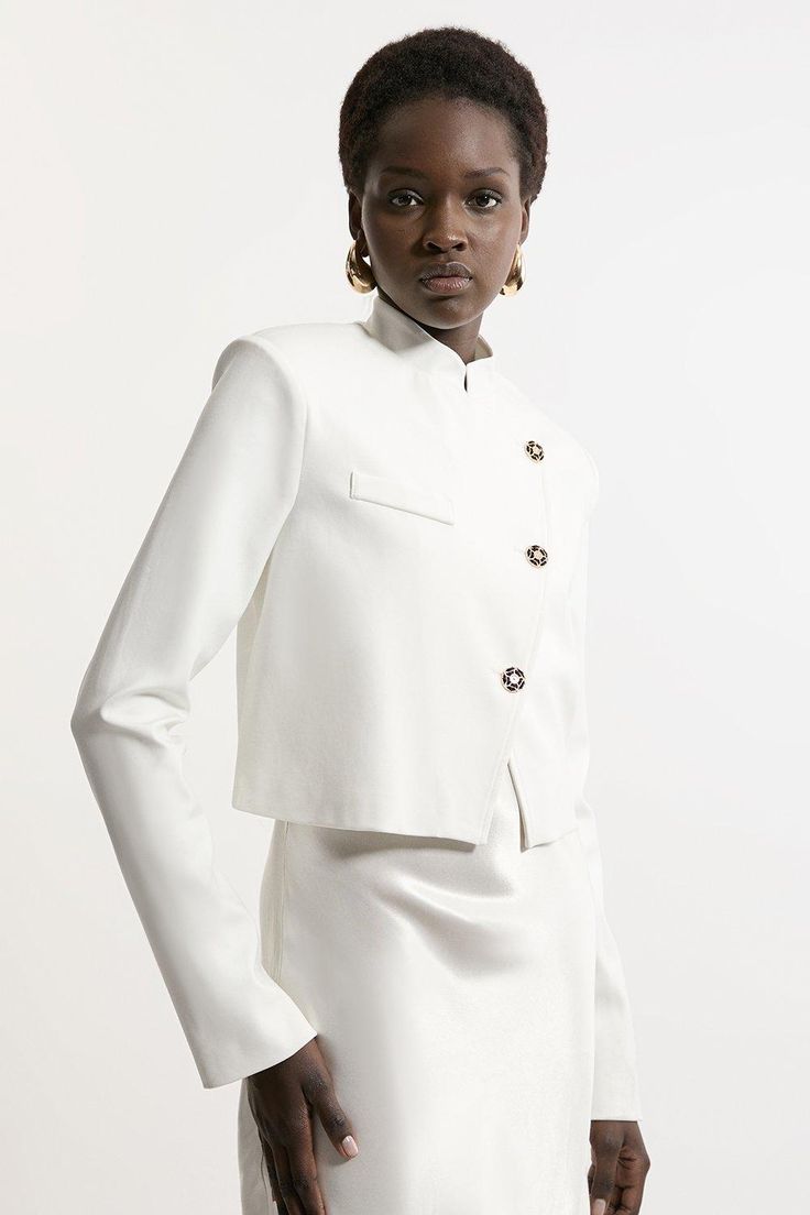 Increase The Formality In Our Cropped Jacket, Which Features A Full-Coverage High Neckline To Protect From The Elements, As Well As A High Collar And A Slightly Cropped Length. Style It With Tailored Trousers And Pointed Toe Heels For A Statement Occasion Look, Perfect For Cool Days That Require An Elevated Look. Button Detail Luxe Ponte Jersey Cropped Jacket Formal High Neckline And Collar Fitted Silhouette Unique Asymmetric Button Detailing Cropped Length Spring Cream Blazer With Button Cuffs, Cream Blazer With Button Cuffs For Spring, Elegant Button-up Cropped Jacket, Fitted White Outerwear With Covered Buttons, Tailored White Cropped Jacket For Spring, Elegant Cream Cropped Jacket For Work, White Chic Cropped Jacket For Formal Occasions, Classic White Cropped Jacket For Work, Elegant Spring Cropped Jacket With Button Cuffs