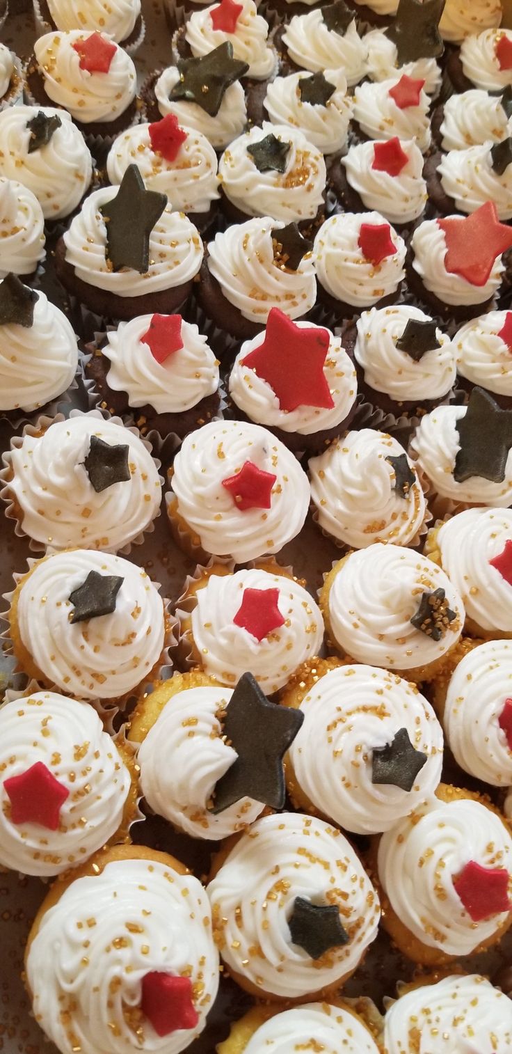 cupcakes with white frosting and red stars on them are arranged in rows