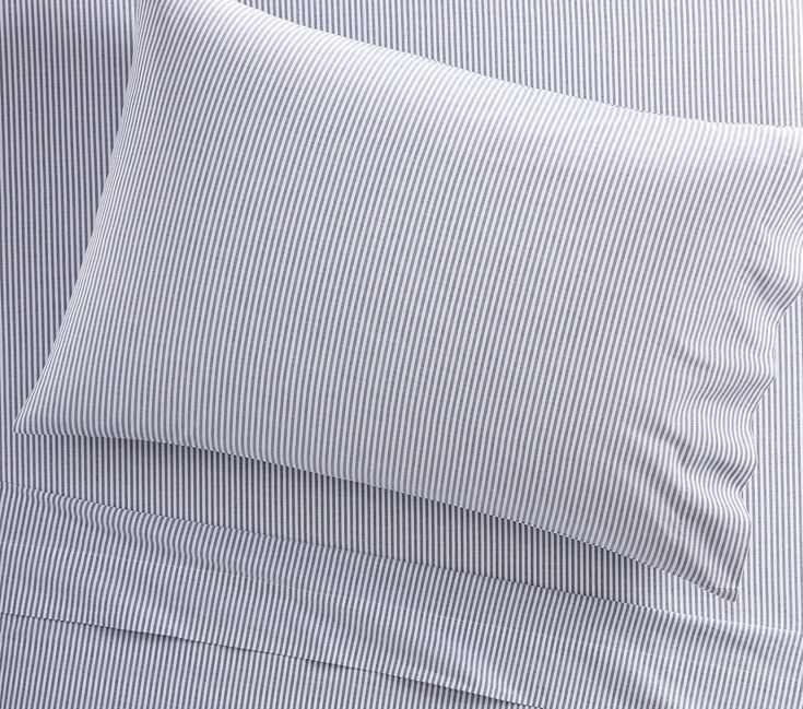 a close up of a bed with white sheets and blue striped pillow cases on it