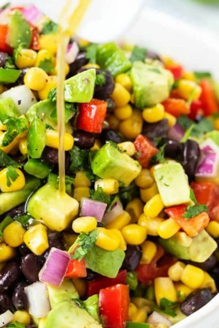 a white bowl filled with black beans, corn and avocado salad topped with cilantro