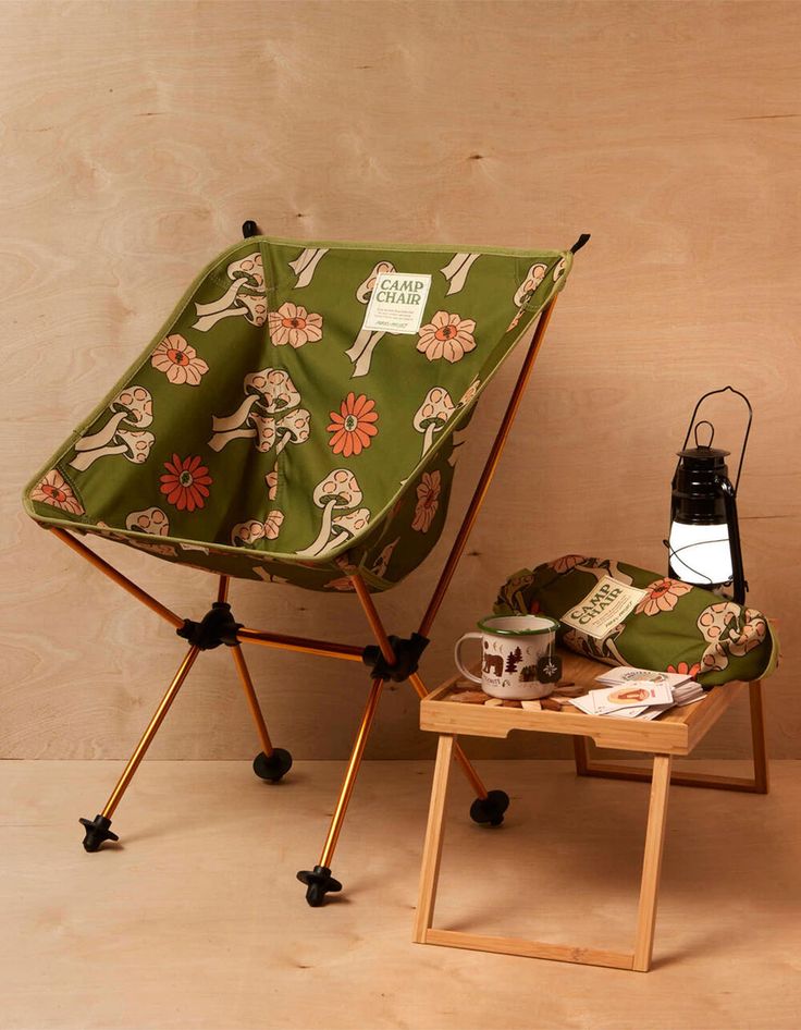 a small table with a lamp on top of it next to a green chair covered in a flowered fabric