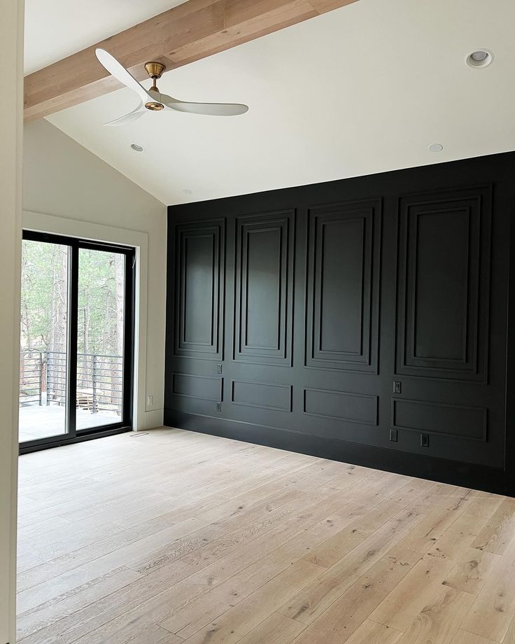 an empty room with black walls and wooden floors, ceiling fan and sliding glass doors