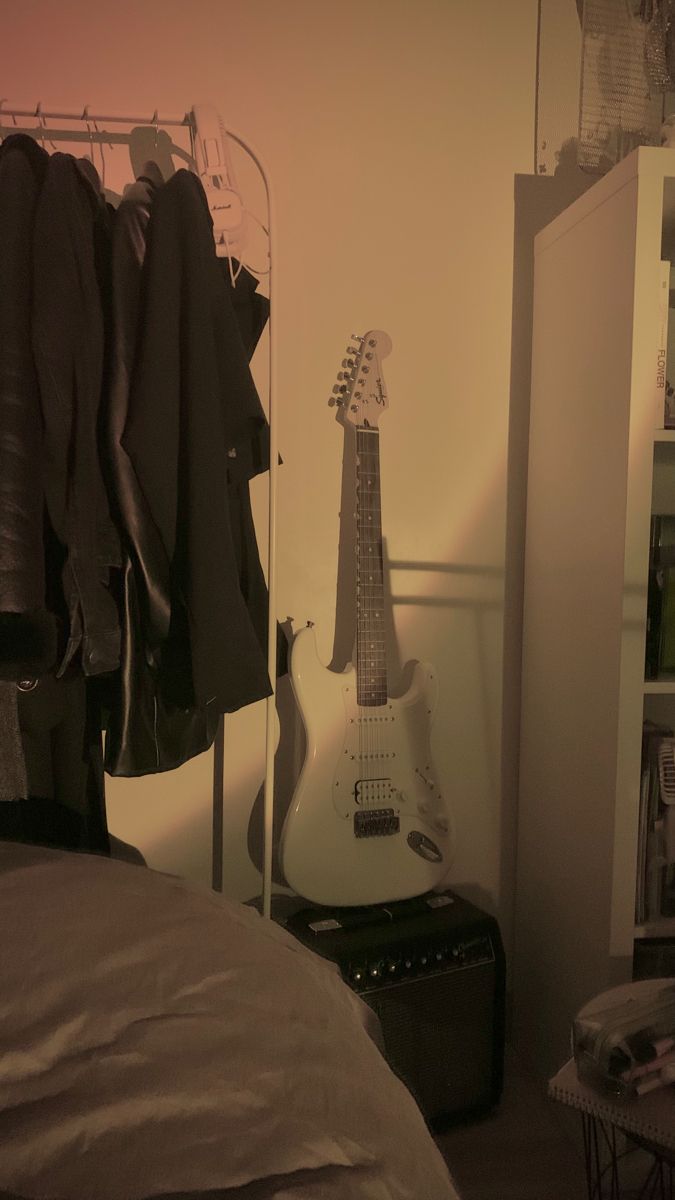 an electric guitar sitting on top of a bed next to a closet filled with clothes