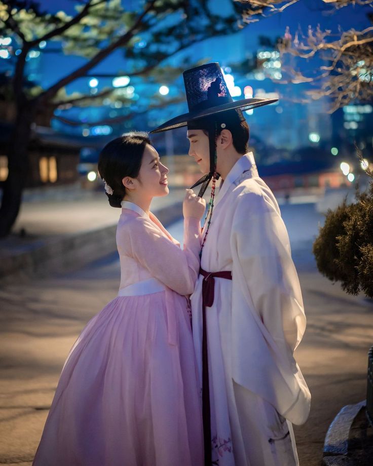 a man and woman dressed in traditional korean clothing standing next to each other on the street