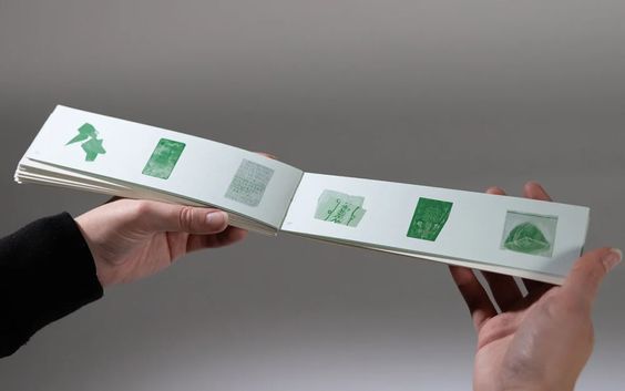 two hands are holding an open book with green stamps on it