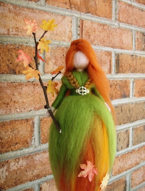 an orange haired doll hanging on a brick wall next to a tree branch with leaves