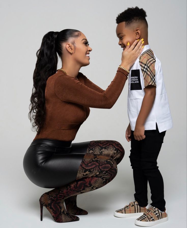 a woman kneeling down next to a little boy who is touching his face with her hand