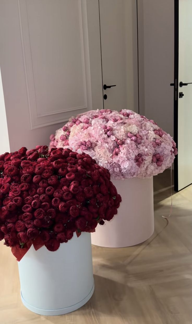 two large white vases filled with flowers on top of a wooden floor next to each other