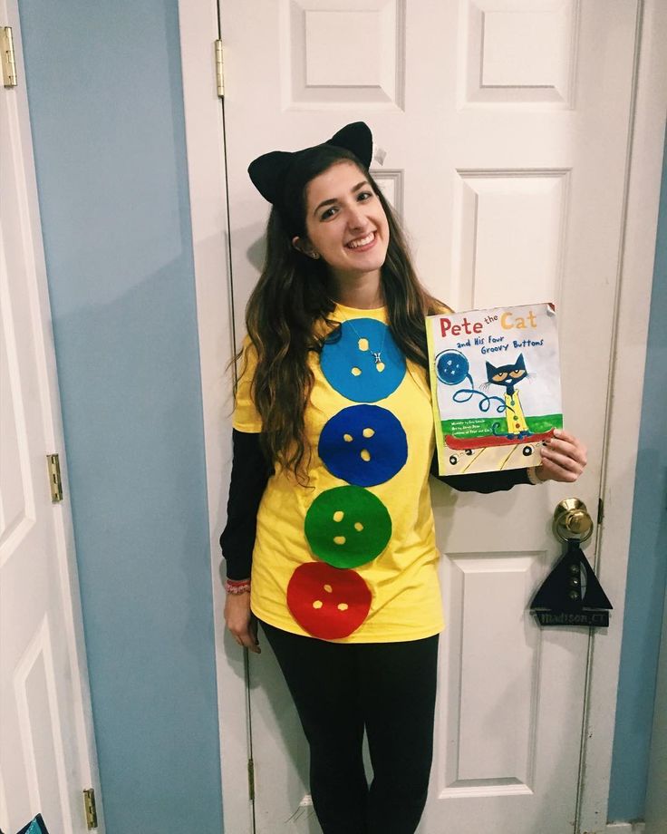 a woman in a costume is standing by a door holding a book and smiling at the camera