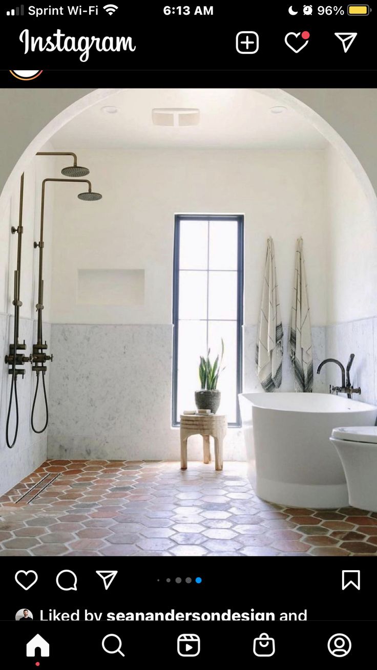 a white bath tub sitting under a window next to a toilet in a room with brick flooring