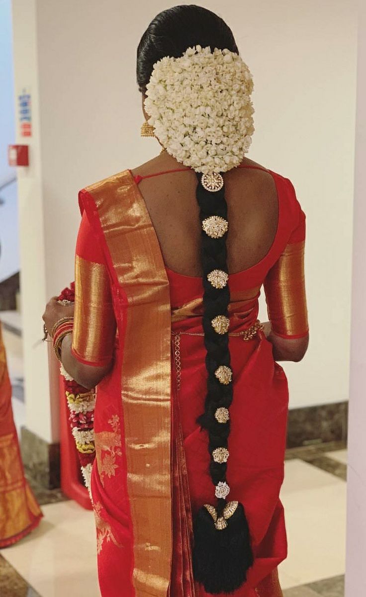 a woman in a red and gold sari with flowers on her head is seen from the back