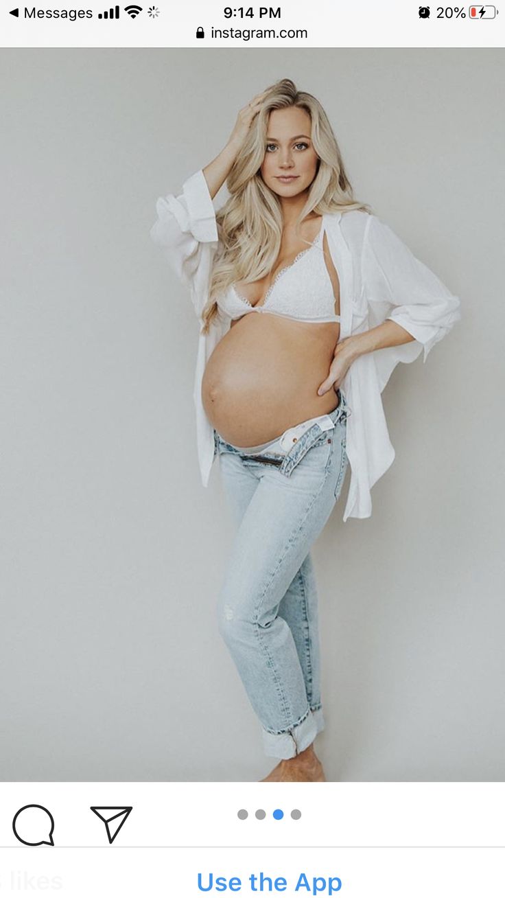 a pregnant woman posing for a photo with her hands on her hips and wearing jeans