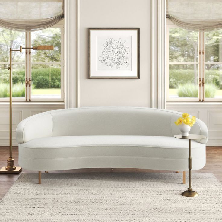 a white couch sitting in front of two windows next to a table with flowers on it