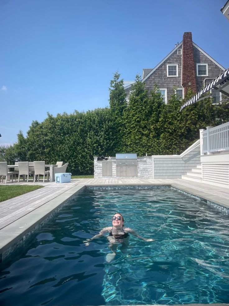 a woman swimming in a pool with clear blue water next to a white fence and house