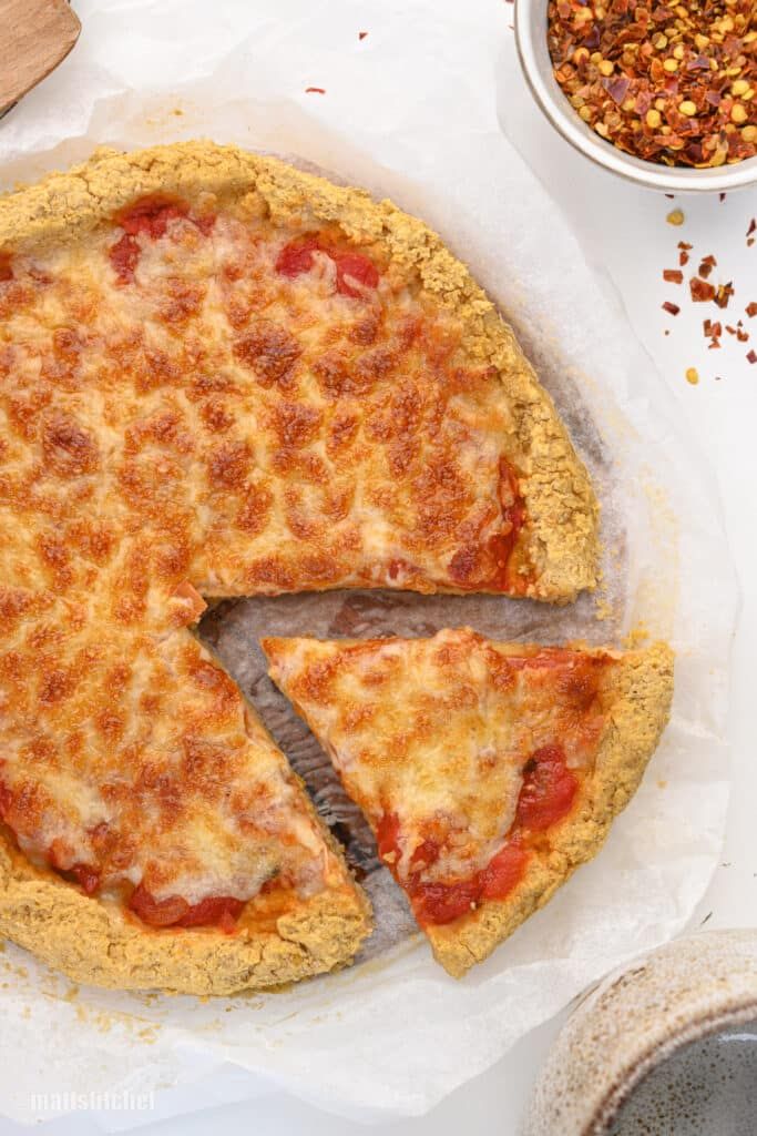 a pizza sitting on top of a white table next to a bowl of chilies