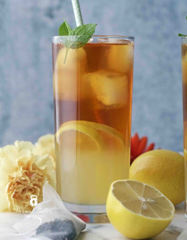 two glasses filled with iced tea and lemons on a table next to some flowers