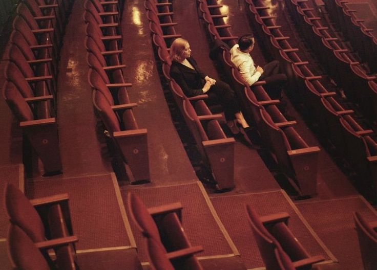 two people are sitting in the middle of an empty auditorium with rows of red seats