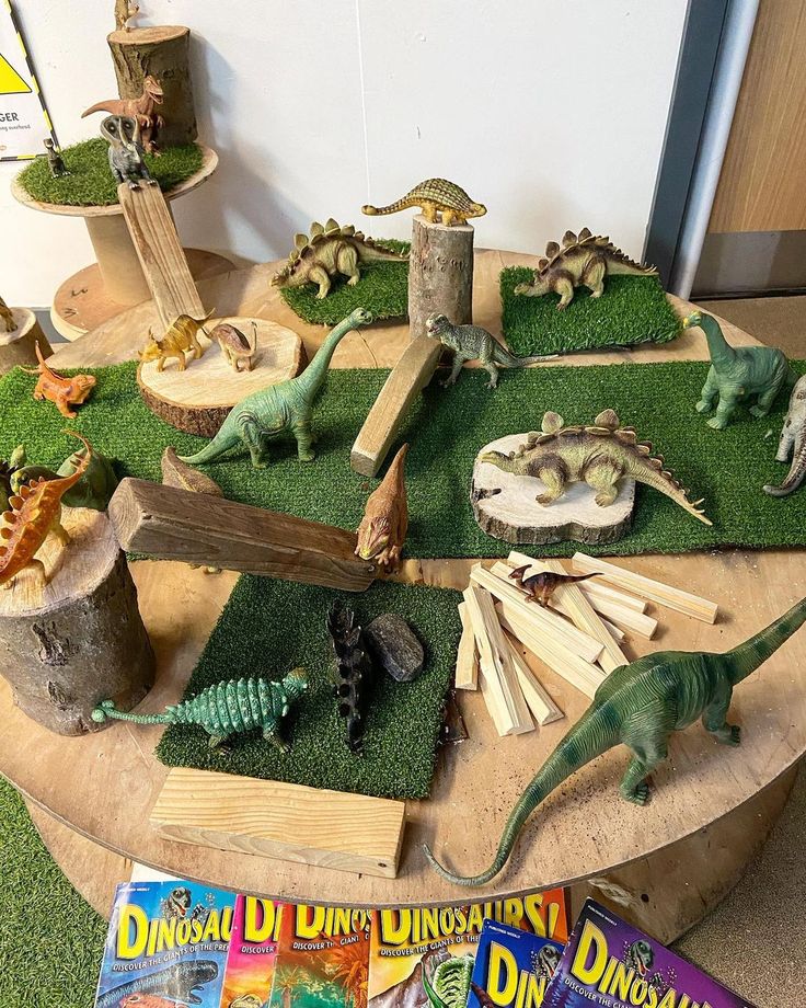 various toy dinosaurs on display in a playroom with fake grass and toys around them