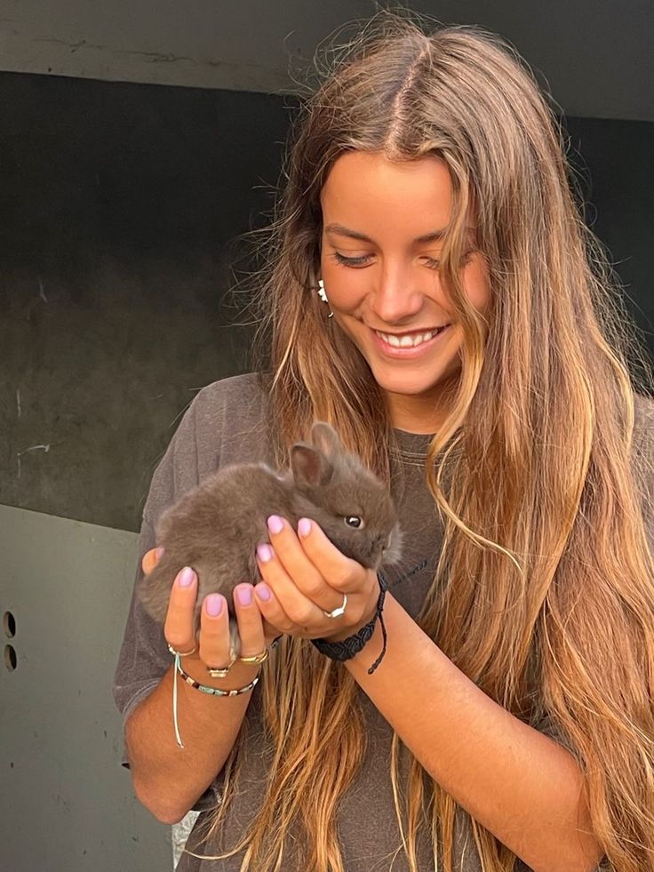 a woman is holding a small animal in her hands and smiling at it's camera