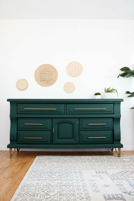 a green dresser with gold handles and brass pulls in a white living room, decorated with potted plants