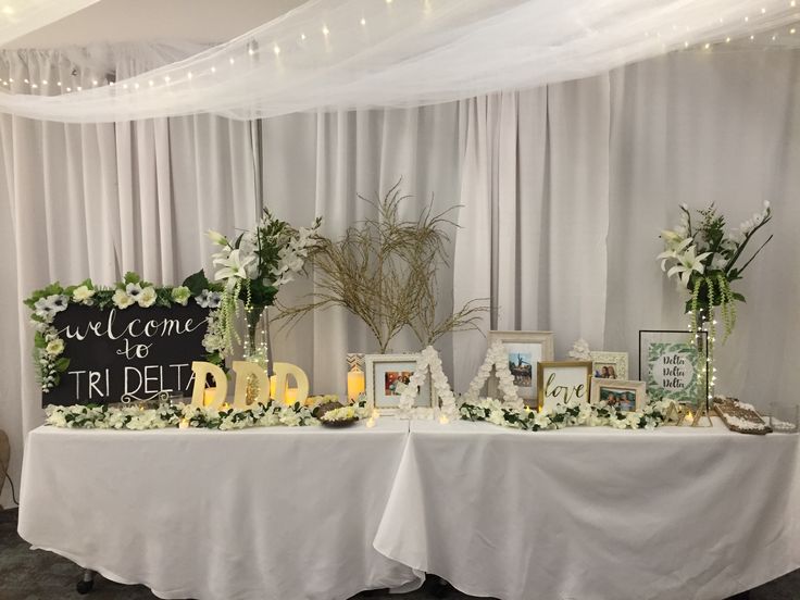 a table topped with pictures and flowers next to a white curtain