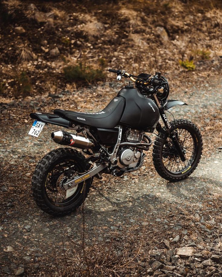 a motorcycle parked on the side of a dirt road next to some rocks and trees