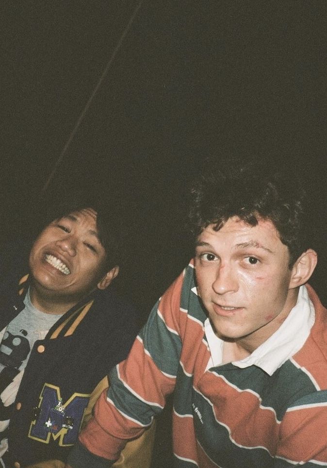 two young men sitting next to each other in front of a dark background, one smiling at the camera