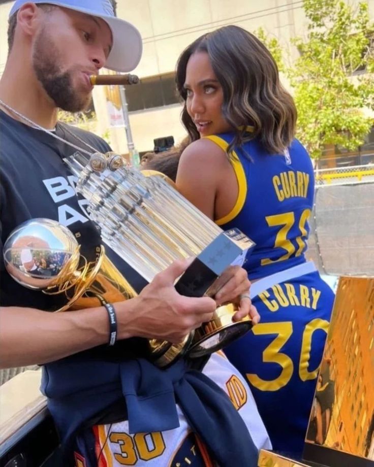 a man and woman standing next to each other in front of a bench holding trophies