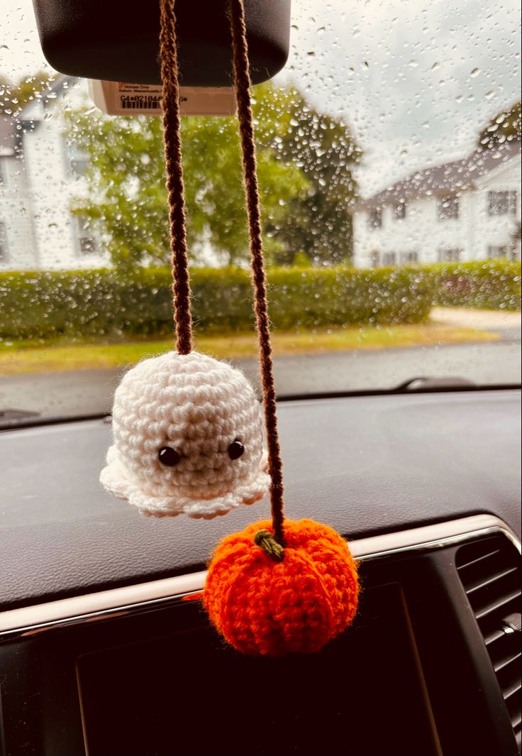 a crocheted pumpkin hanging from the dashboard of a car with raindrops