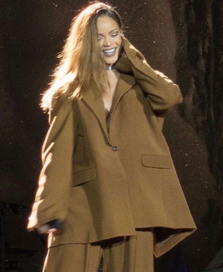 a woman with long hair wearing a tan suit and smiling while talking on her cell phone