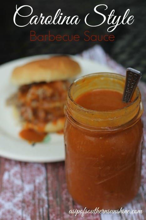 a jar of barbecue sauce sitting next to a sandwich on a plate with a spoon in it