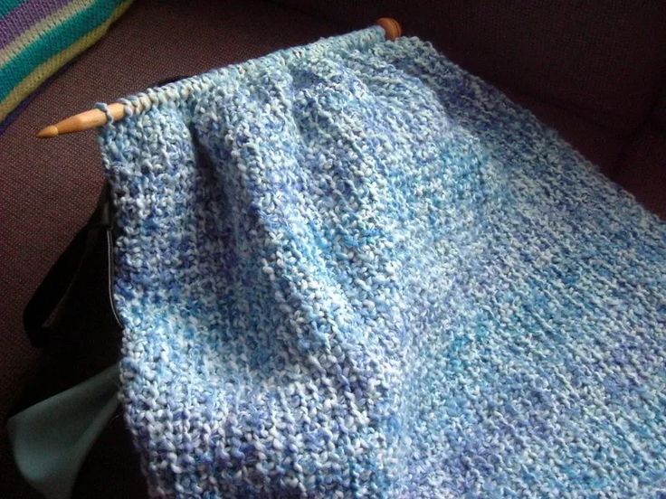 a blue knitted blanket sitting on top of a couch next to a wooden stick