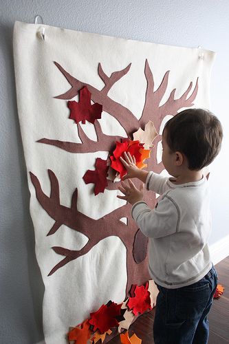 a little boy that is standing in front of a wall hanging with leaves on it