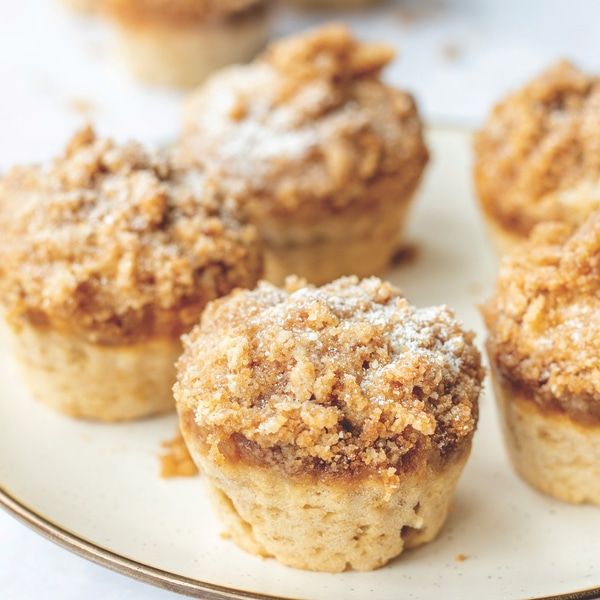 three small muffins on a plate with powdered sugar and crumbs