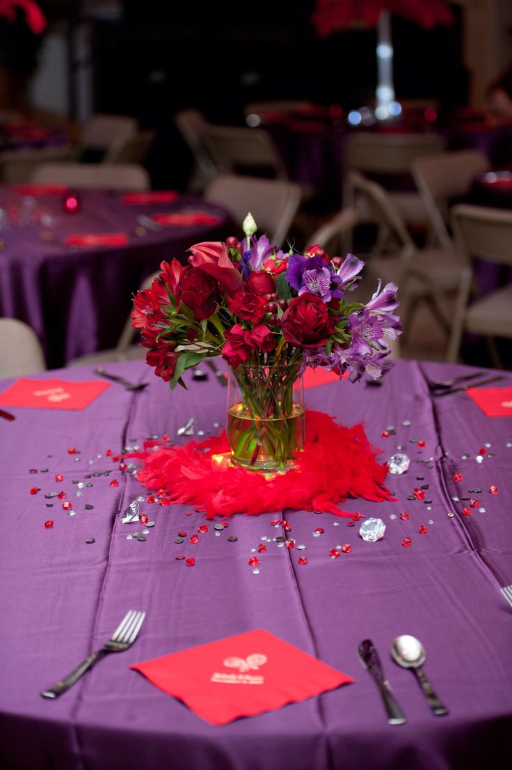 a vase filled with red and purple flowers on top of a table covered in confetti