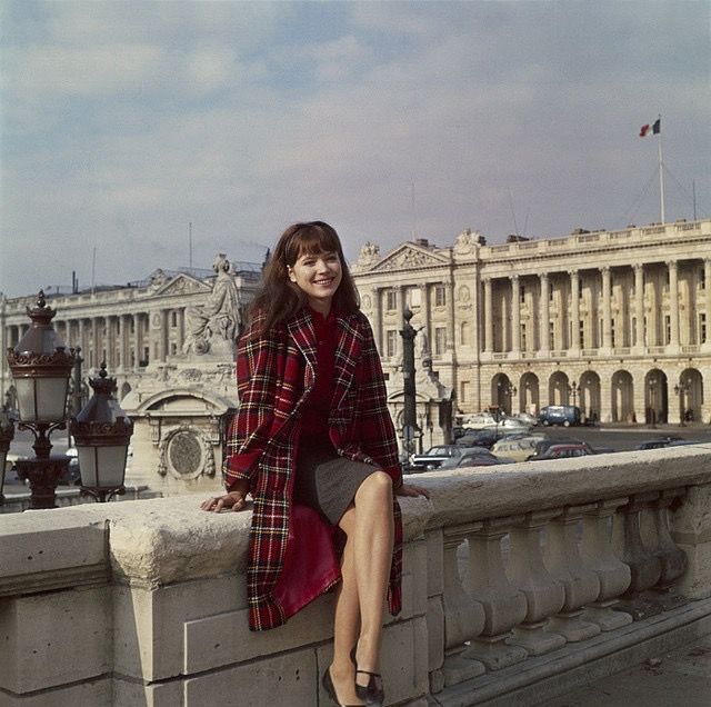 a woman sitting on top of a stone wall next to a building with a clock tower in the background