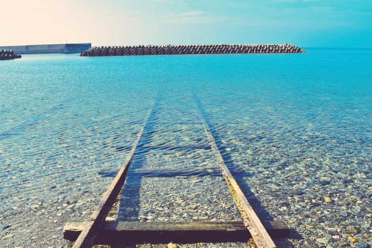 an old wooden boat sitting on top of a beach next to the ocean and jetty