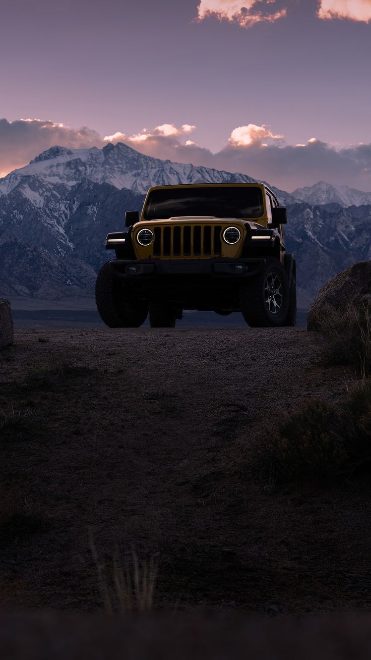 a yellow jeep parked in the desert with mountains in the back ground and clouds in the sky