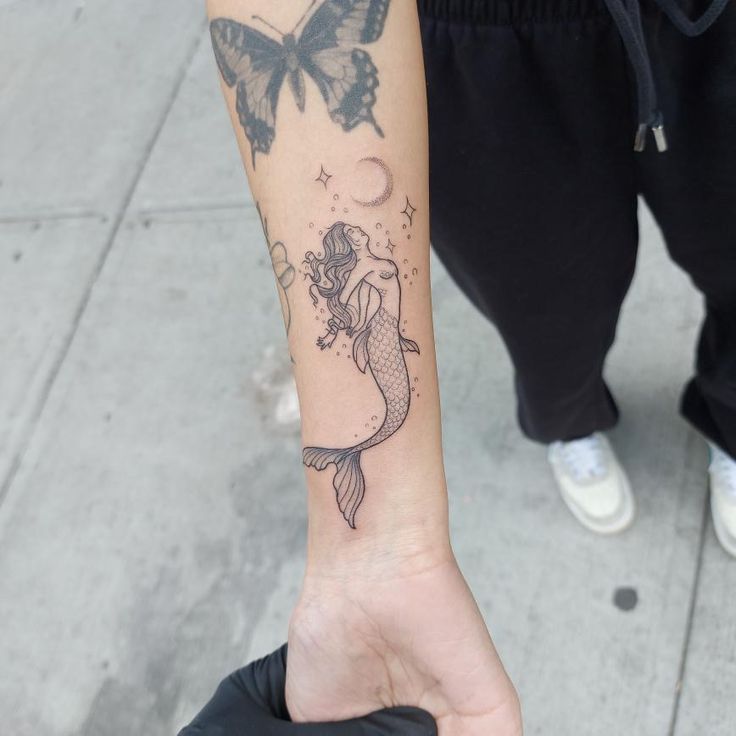 a person with a tattoo on their arm holding a butterfly and a fish in the air